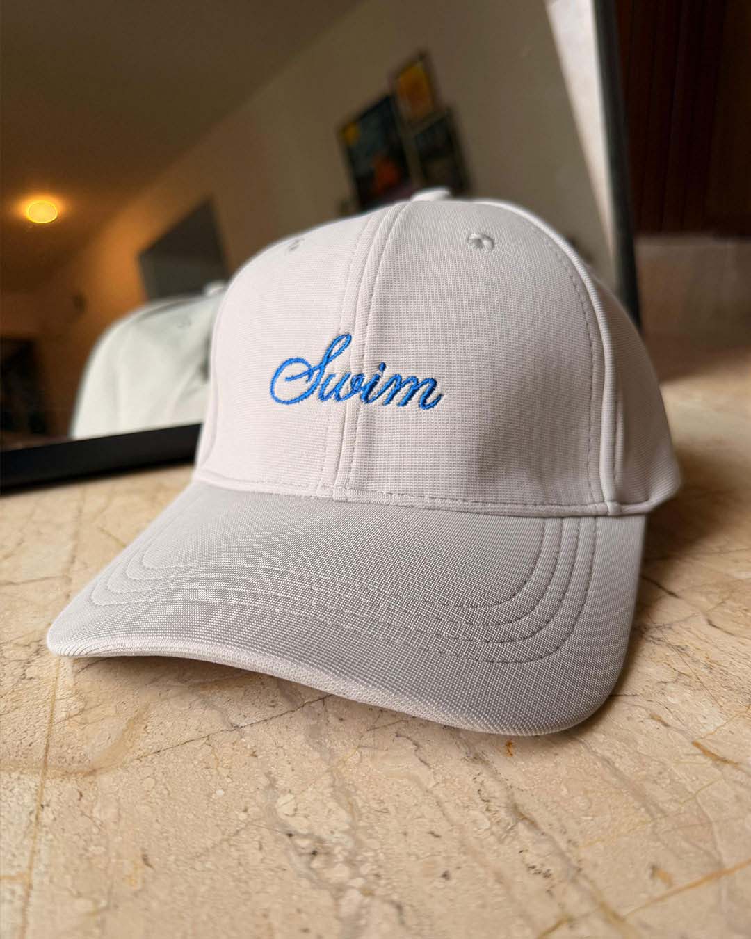 White cap with 'Swim' embroidered on it, placed on a wooden floor.